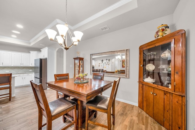 dining area featuring a tray ceiling, crown molding, a notable chandelier, light wood finished floors, and visible vents