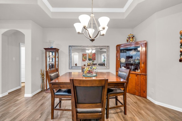 dining space with arched walkways, light wood finished floors, and a raised ceiling