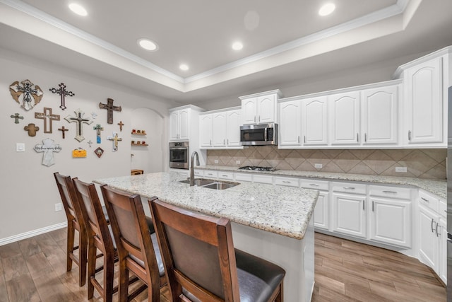 kitchen featuring a tray ceiling, stainless steel appliances, light wood-style floors, a kitchen bar, and a sink