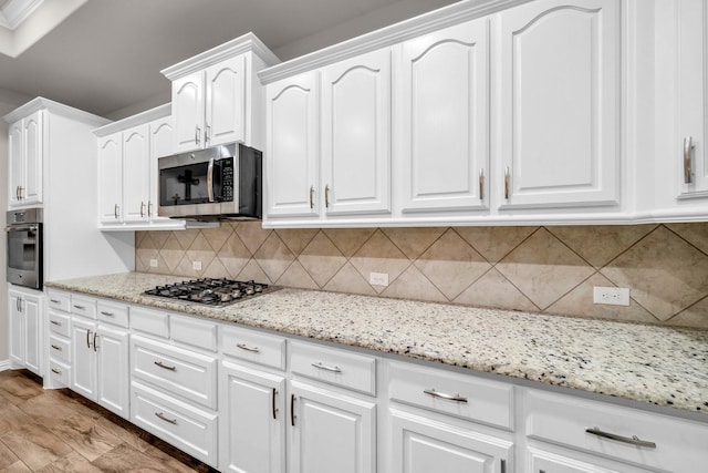 kitchen with light stone counters, stainless steel appliances, tasteful backsplash, white cabinets, and wood finished floors