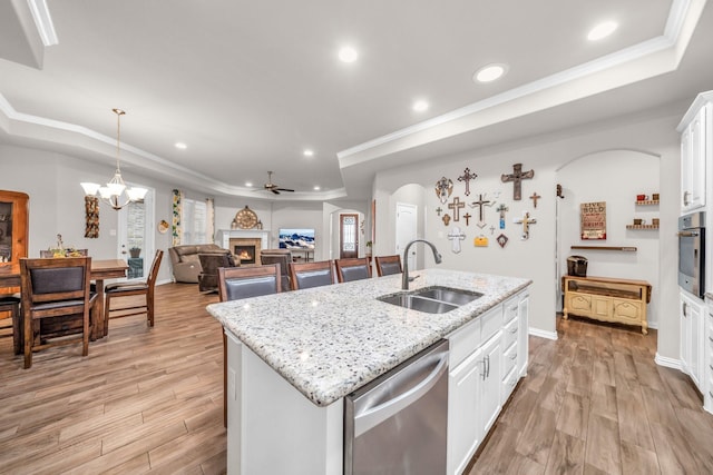 kitchen with a warm lit fireplace, light wood finished floors, a tray ceiling, stainless steel appliances, and a sink