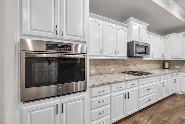 kitchen with stainless steel appliances, white cabinetry, light stone countertops, dark wood-style floors, and tasteful backsplash