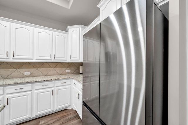 kitchen with light wood finished floors, stainless steel refrigerator, white cabinetry, and decorative backsplash