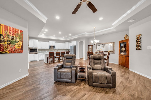 living area with arched walkways, ornamental molding, a raised ceiling, and light wood-style flooring