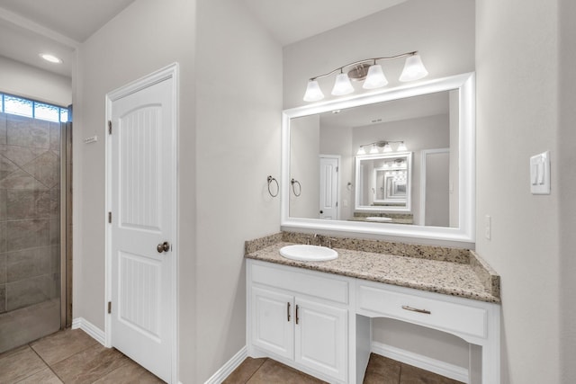 bathroom with tile patterned flooring, tiled shower, vanity, and baseboards