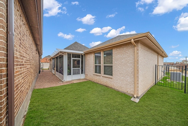 rear view of property featuring a sunroom, brick siding, a lawn, and a fenced backyard