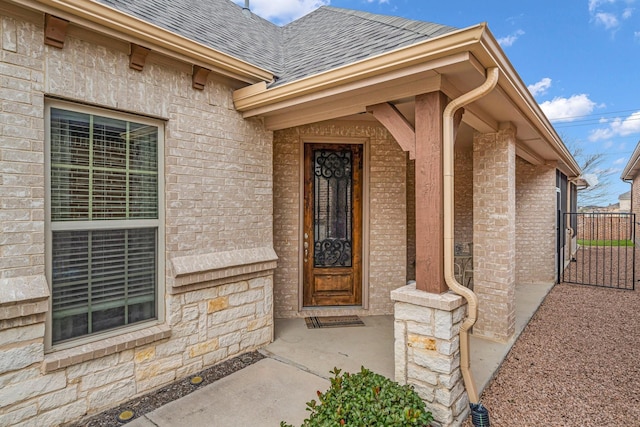 property entrance featuring brick siding, a gate, and roof with shingles