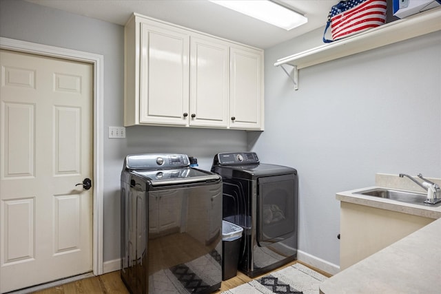 clothes washing area with baseboards, light wood-type flooring, separate washer and dryer, cabinet space, and a sink