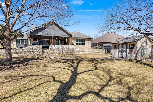 rear view of house with brick siding, a fenced front yard, a lawn, an outbuilding, and a storage unit