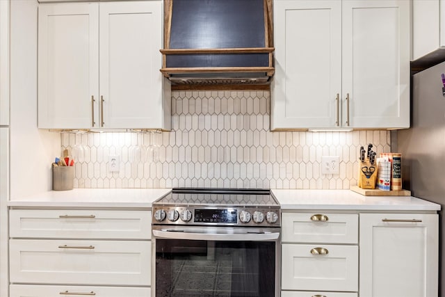 kitchen with custom exhaust hood, stainless steel electric stove, light countertops, white cabinets, and tasteful backsplash