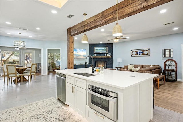 kitchen with a sink, appliances with stainless steel finishes, decorative light fixtures, open floor plan, and a large fireplace