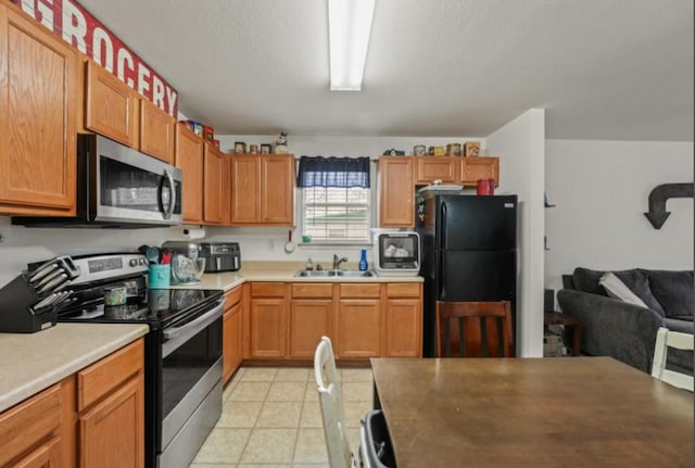 kitchen with stainless steel appliances, light countertops, open floor plan, light tile patterned flooring, and a sink