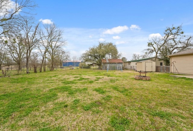 view of yard featuring a fire pit, a storage unit, fence, and an outbuilding