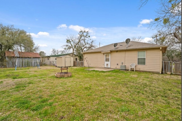 rear view of house with a storage shed, a fire pit, a fenced backyard, an outbuilding, and a patio area