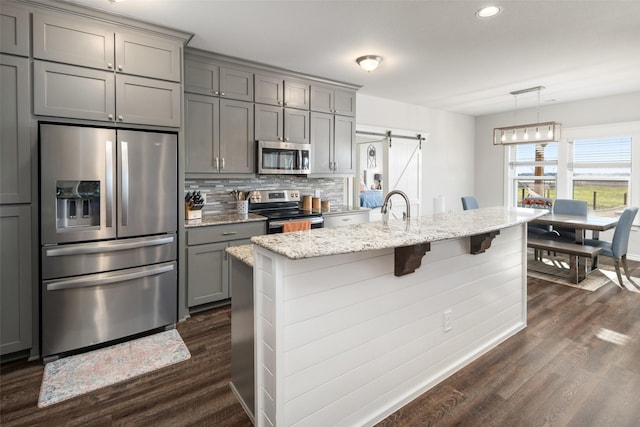 kitchen with a barn door, gray cabinets, stainless steel appliances, and dark wood-style flooring