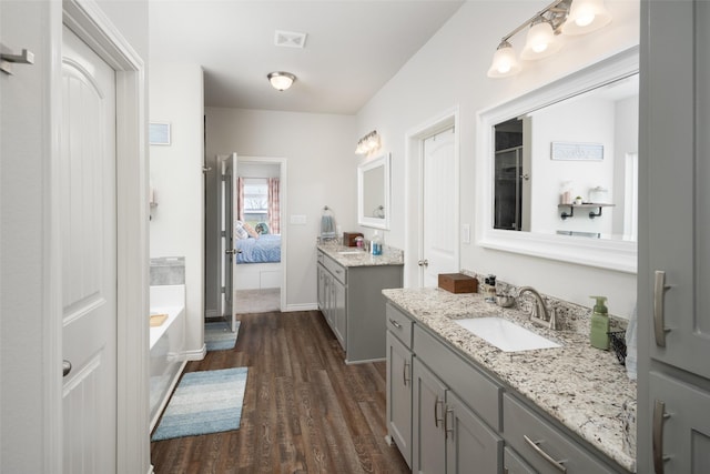 full bath with ensuite bath, wood finished floors, a sink, a garden tub, and two vanities