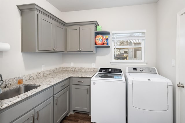 clothes washing area featuring dark wood finished floors, cabinet space, a sink, and washer and clothes dryer