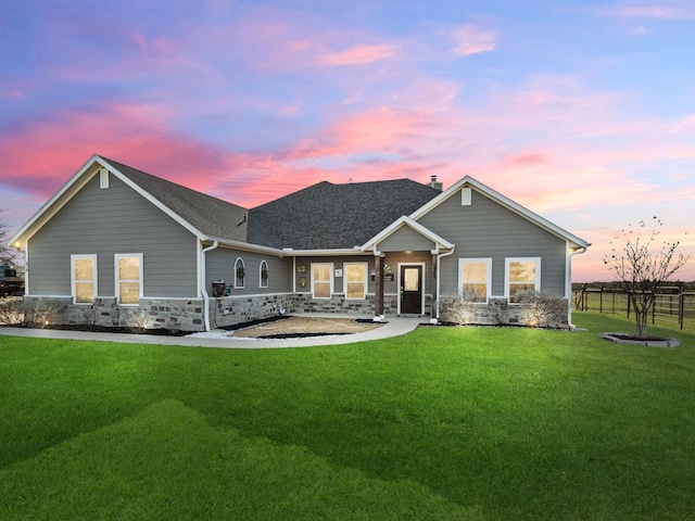 view of front of home with stone siding, a shingled roof, fence, and a front yard