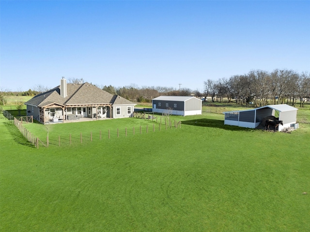 view of yard with a patio area, fence, an outbuilding, and a rural view