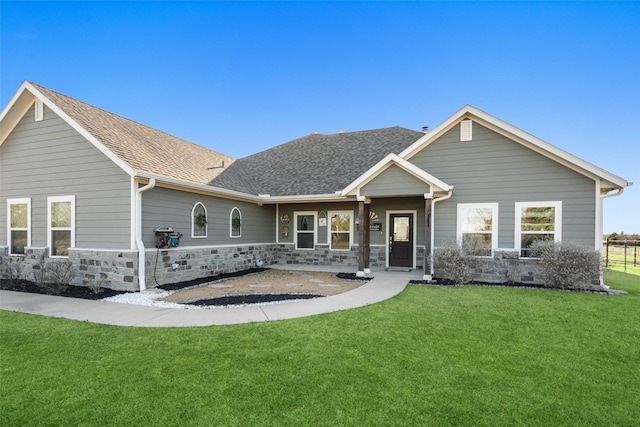 view of front facade featuring stone siding, roof with shingles, and a front yard