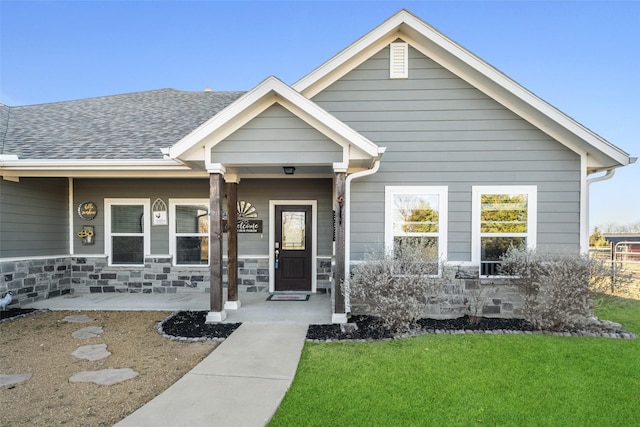 doorway to property featuring stone siding, a lawn, and roof with shingles