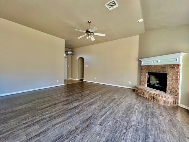 unfurnished living room with visible vents, arched walkways, dark wood finished floors, ceiling fan, and a fireplace