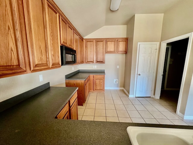 2436 Castle Pines Dr, Burleson, TX 76028 - kitchen featuring light tile patterned floors, dark countertops, brown cabinetry, vaulted ceiling, and black microwave