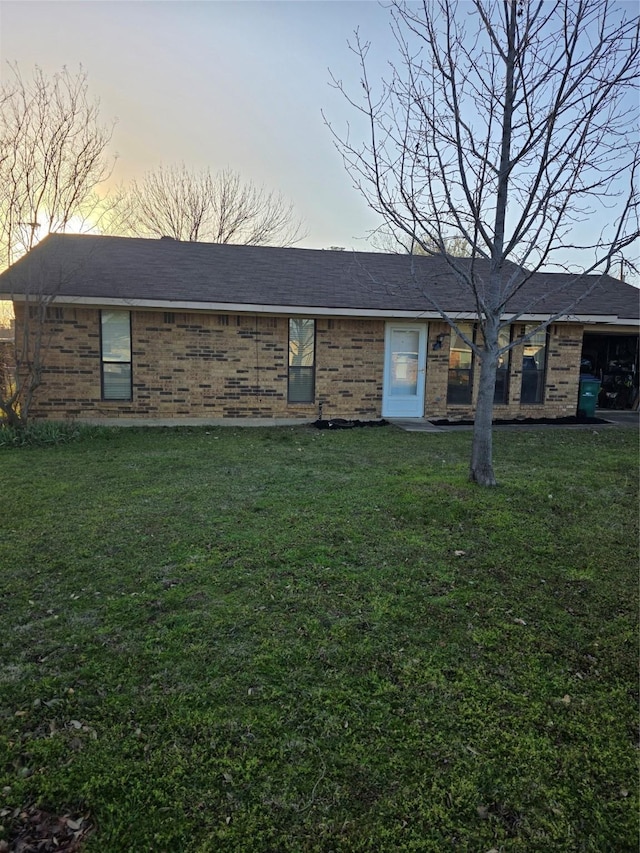 view of front facade with a lawn, roof with shingles, and brick siding