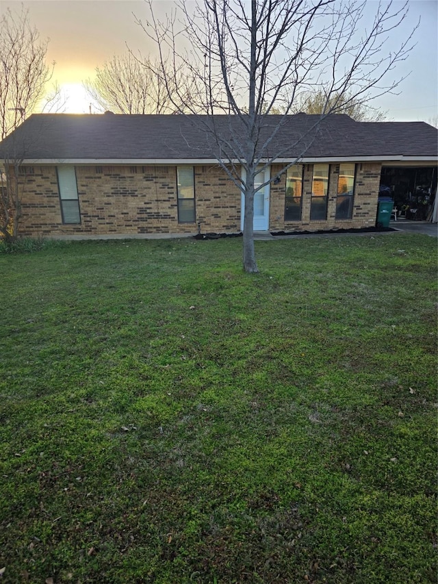 view of front of property featuring an attached carport, a yard, brick siding, and a shingled roof