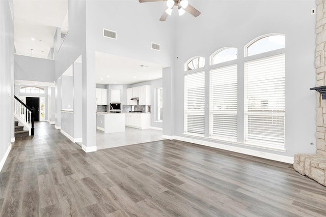 unfurnished living room with stairs, a healthy amount of sunlight, visible vents, and light wood-style floors