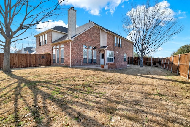 back of property featuring brick siding, a yard, a chimney, a patio area, and a fenced backyard