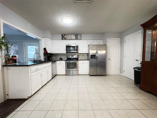 kitchen with dark countertops, decorative backsplash, appliances with stainless steel finishes, light tile patterned flooring, and a sink