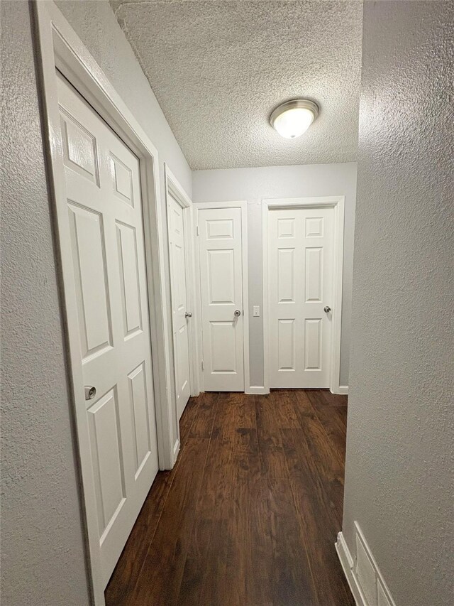 hall featuring dark wood finished floors, visible vents, a textured wall, a textured ceiling, and baseboards