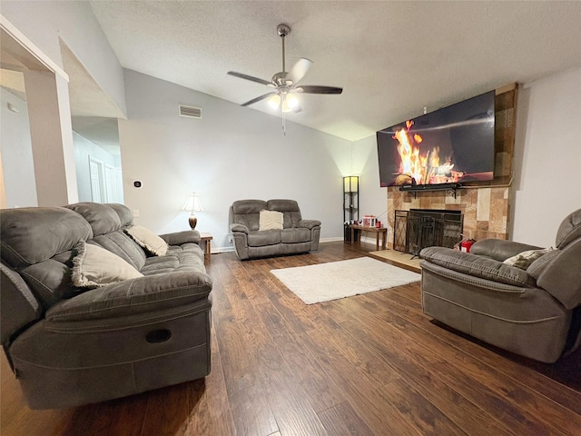 living area with dark wood-style floors, lofted ceiling, visible vents, a tiled fireplace, and a textured ceiling