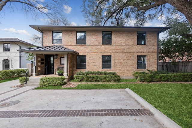 view of front of house featuring a standing seam roof, brick siding, a front yard, and fence