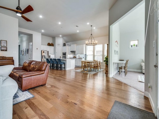 living area featuring recessed lighting, baseboards, lofted ceiling, light wood-type flooring, and ceiling fan with notable chandelier