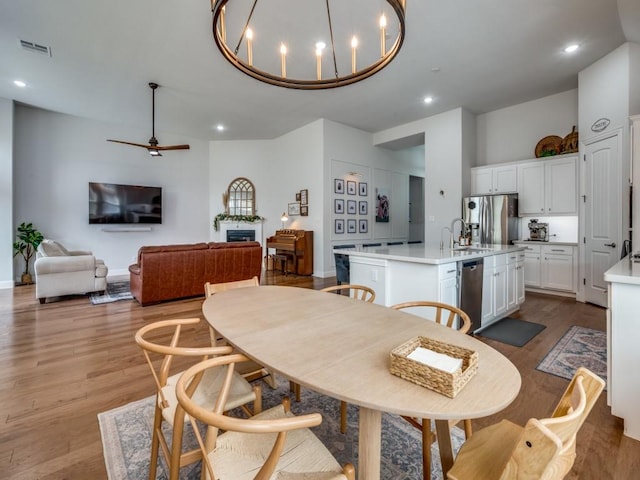 dining room with light wood finished floors, visible vents, ceiling fan with notable chandelier, a fireplace, and recessed lighting