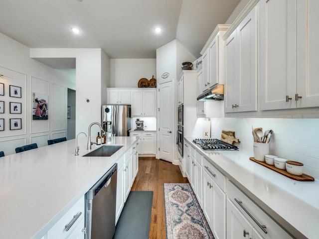 kitchen with decorative backsplash, stainless steel appliances, light countertops, under cabinet range hood, and a sink