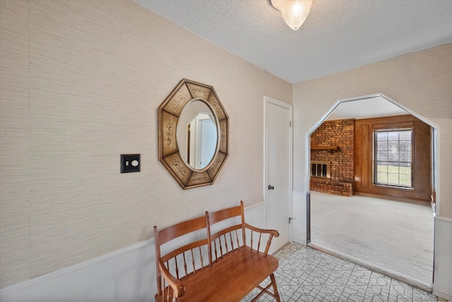 hall featuring wallpapered walls, a textured ceiling, and light colored carpet