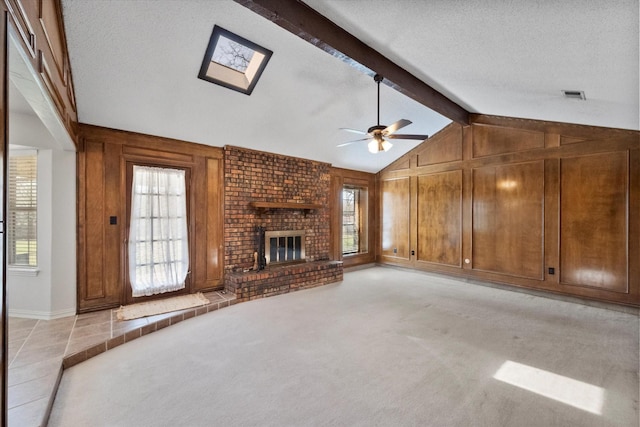 unfurnished living room featuring a brick fireplace, light carpet, wood walls, a textured ceiling, and vaulted ceiling with skylight