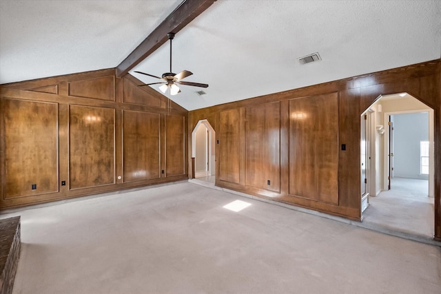 spare room with light colored carpet, arched walkways, visible vents, and wood walls