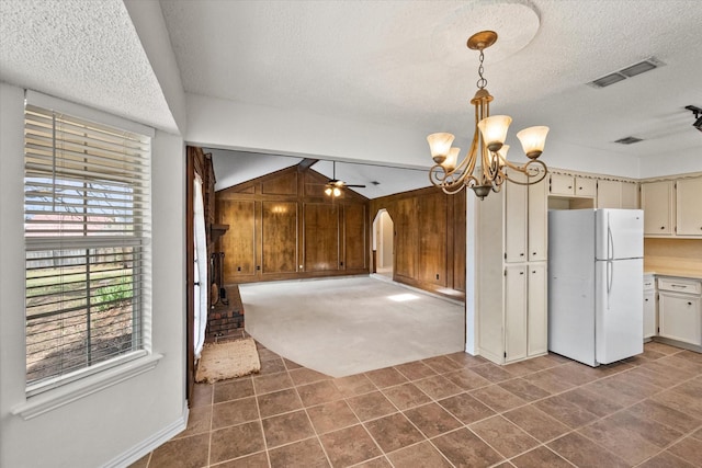 kitchen featuring lofted ceiling, a textured ceiling, wood walls, visible vents, and freestanding refrigerator