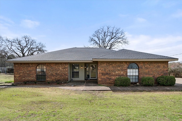 view of front of property featuring brick siding, roof with shingles, and a front yard