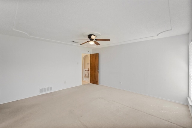 carpeted spare room featuring arched walkways, ceiling fan, and visible vents