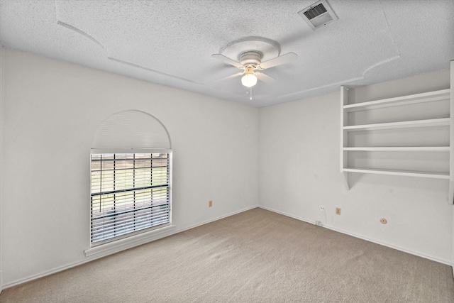 unfurnished room featuring a textured ceiling, carpet floors, visible vents, and a ceiling fan