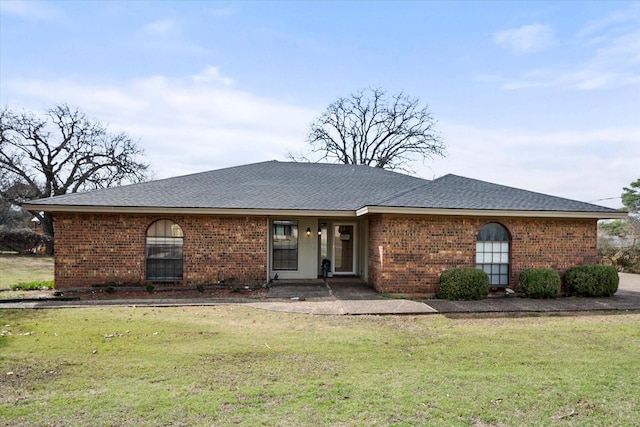 view of front of house with a shingled roof, a front yard, and brick siding