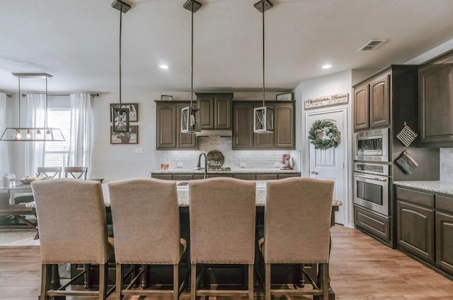 713 Falcon Rd, Argyle, TX 76226 - kitchen with appliances with stainless steel finishes, backsplash, a kitchen breakfast bar, an island with sink, and light wood-style floors