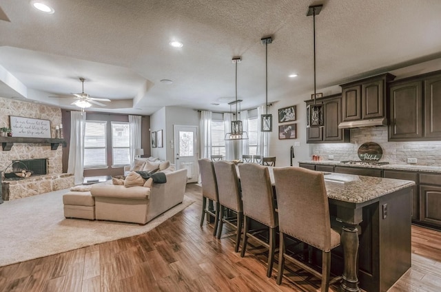 kitchen with a kitchen breakfast bar, open floor plan, a kitchen island, a raised ceiling, and wood finished floors