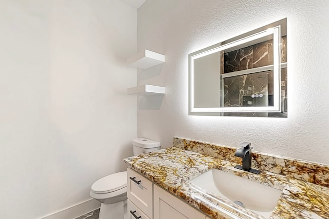 bathroom featuring toilet, a textured wall, and vanity