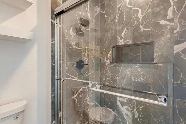 bathroom featuring toilet and a marble finish shower